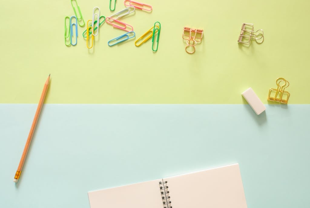 Assorted-color Metal Clips on Table Beside Pencil and Notebook
