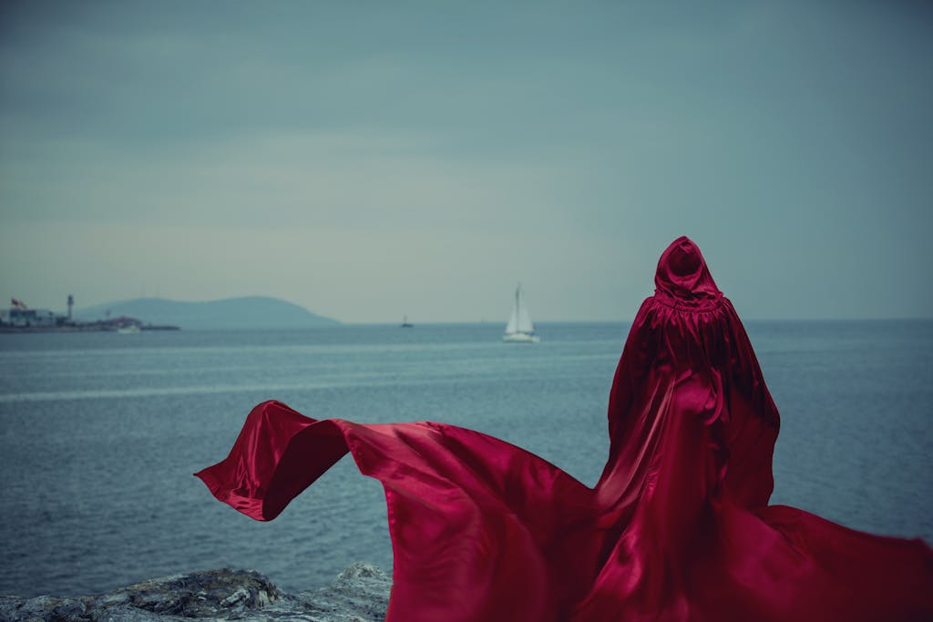 Woman in a Long Red Cloak with a Hood at the Edge of a Cliff